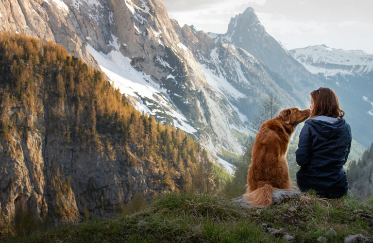 A woman and a dog sitting together on a mountain