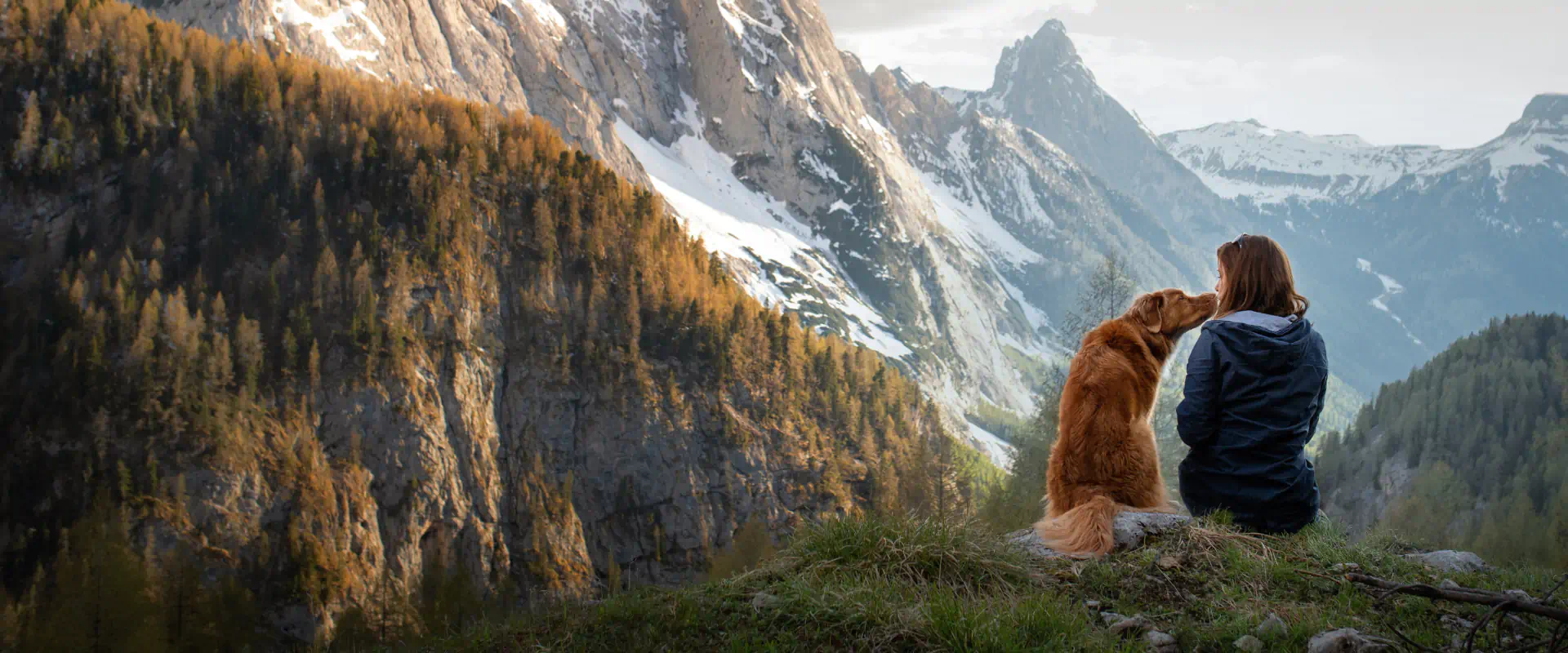 A woman and a dog sitting together on a mountain