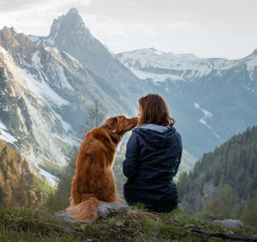 A woman and a dog sitting together on a mountain
